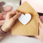 womans hands holding a letter in craft envelope pink background valentines day concept tulips